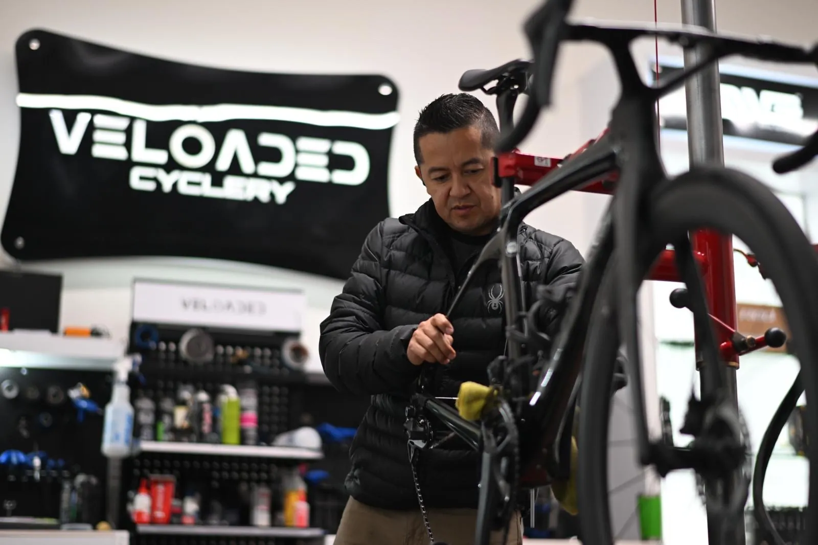 Edgar Rodriguez working on a road bike under the Veloaded Cyclery wall sign